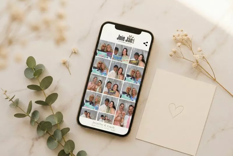 Smartphone displaying Joie Jae Memory Booth content gallery with photo grid, surrounded by dried flowers and eucalyptus on marble surface